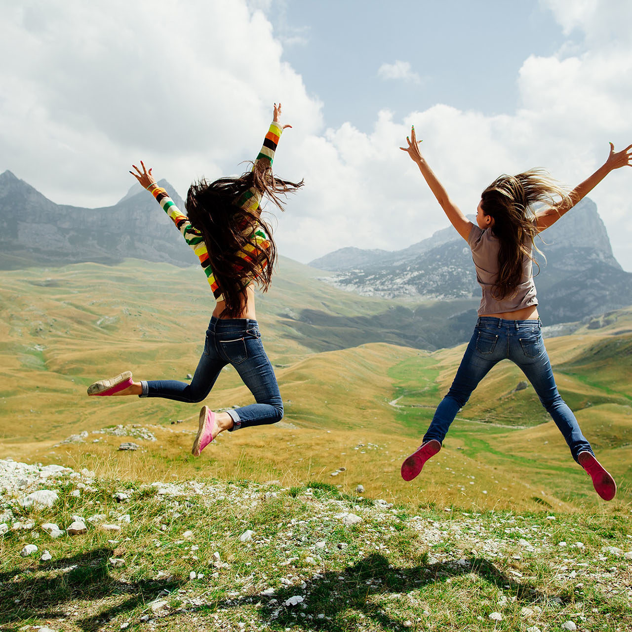 two long hair girls happy jump in mountains with exciting view of Montenegro, Durmitor, back view